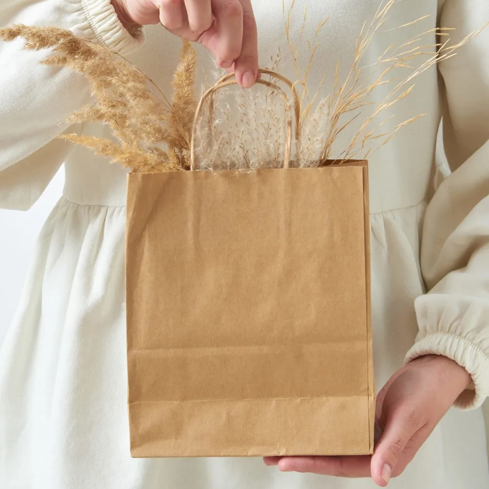 Womans hand holding paper eco bag with dry natural plant twig - Hidalgo-werbeartikel Papieren kraft tas 90g/m² 18x8x22cm — productfoto 7